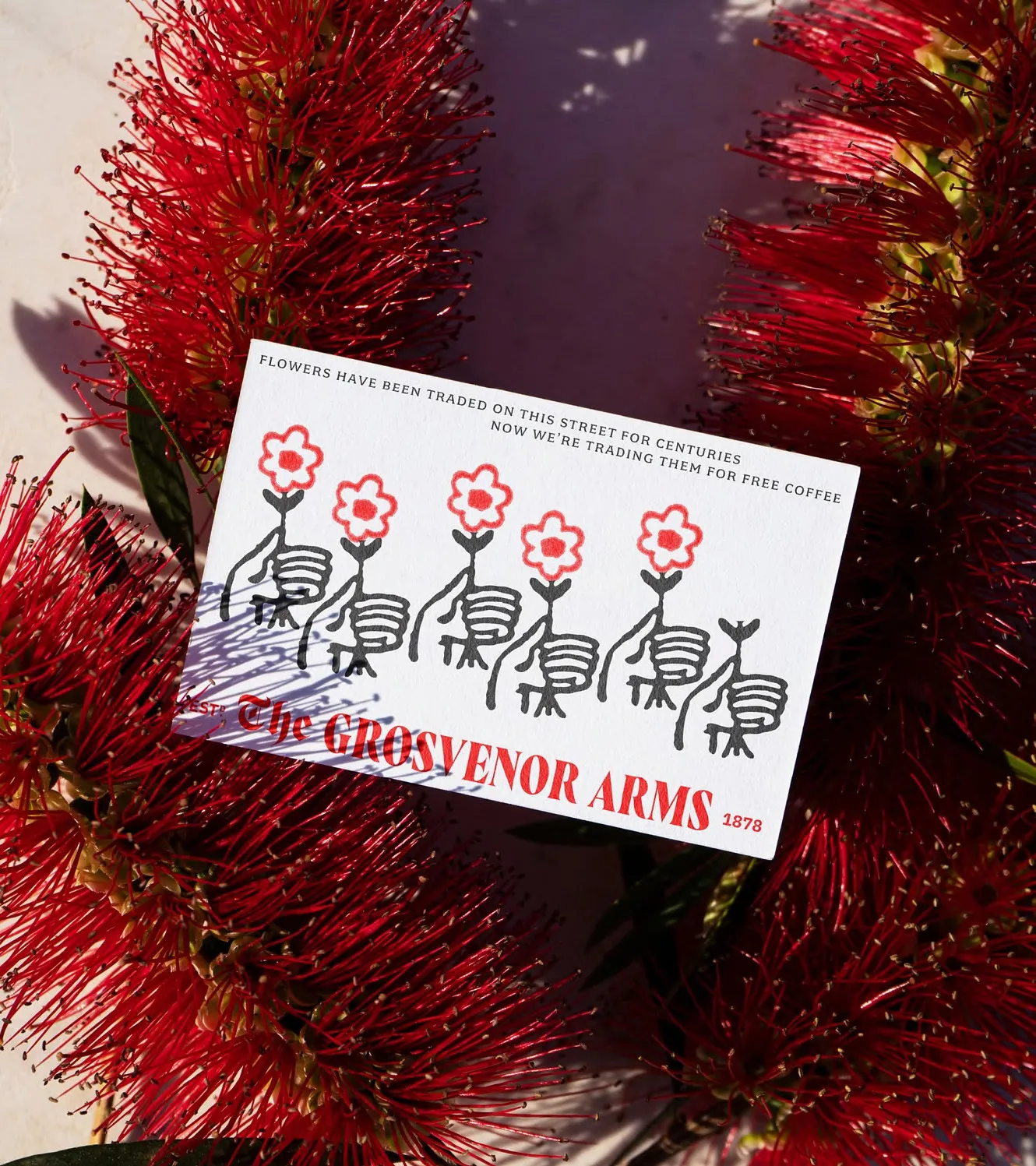A Grosvenor Arms card reading "flowers have been traded on this street for centuries", resting on red bottlebrush flowers